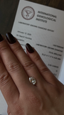 Hand wearing a diamond ring with an International Gemological Institute report in the background