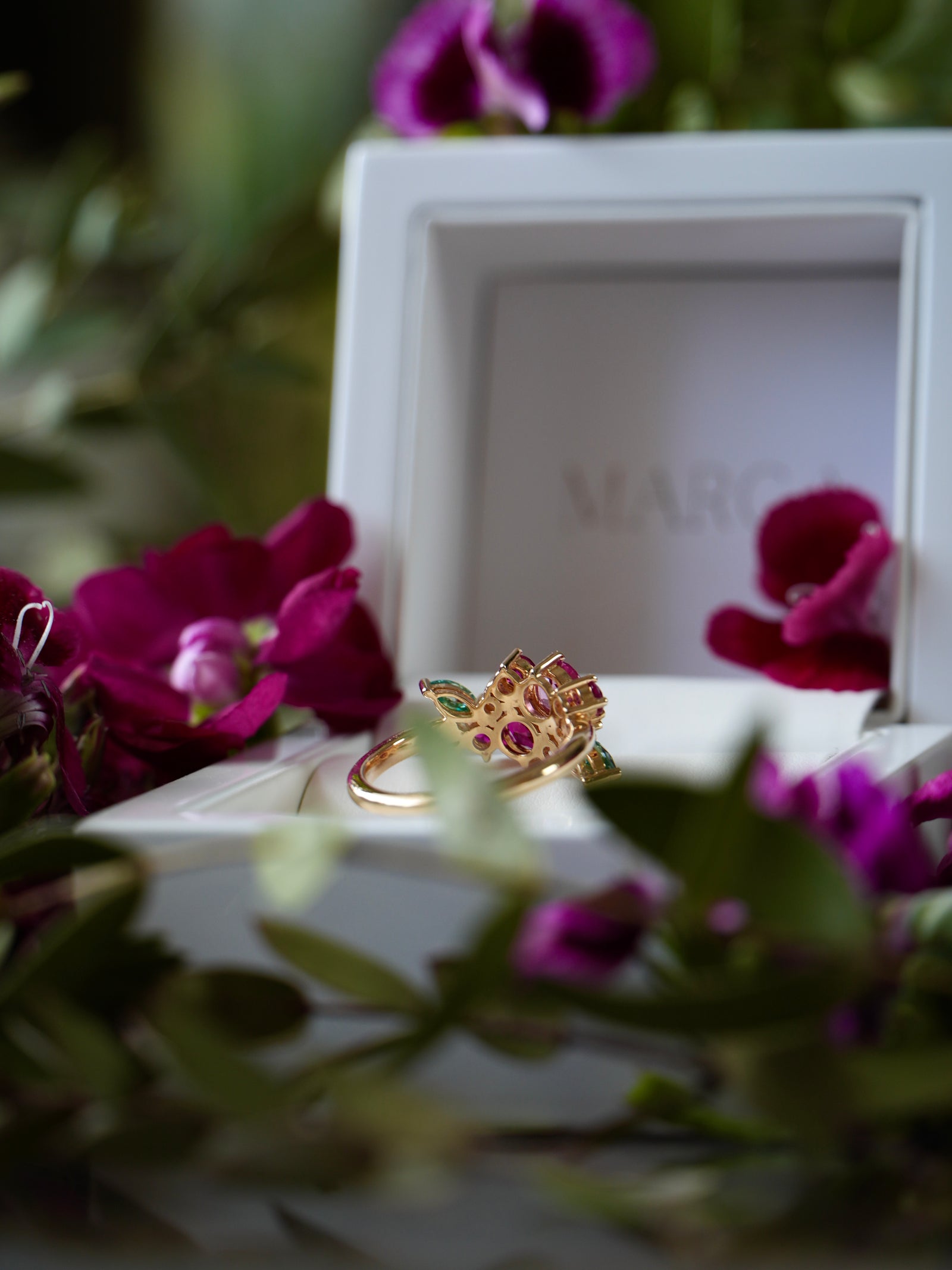 Gold ring with gemstones on a white box surrounded by purple flowers
