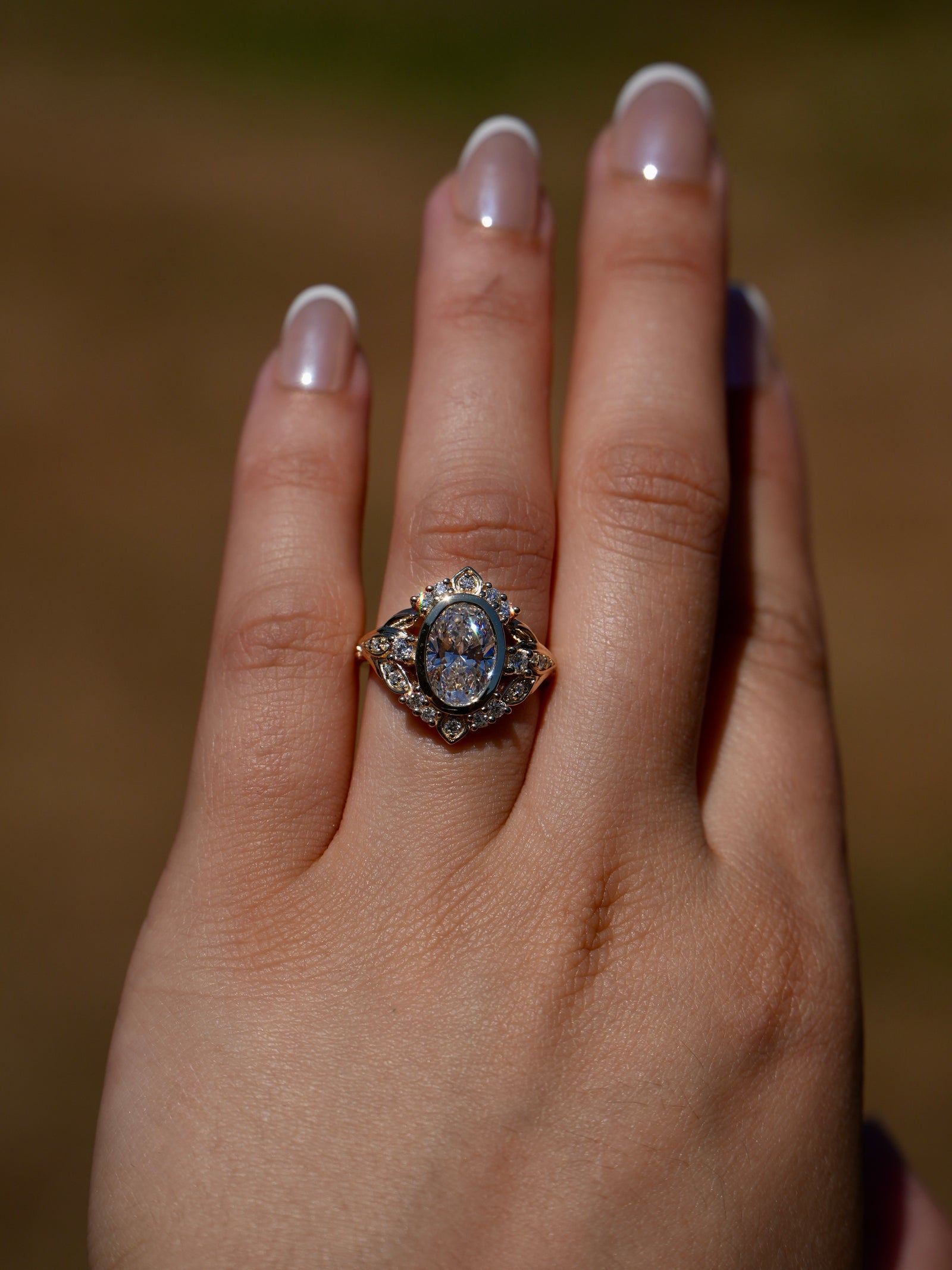 Close-up of a hand wearing an ornate ring with a large gemstone against a blurred background