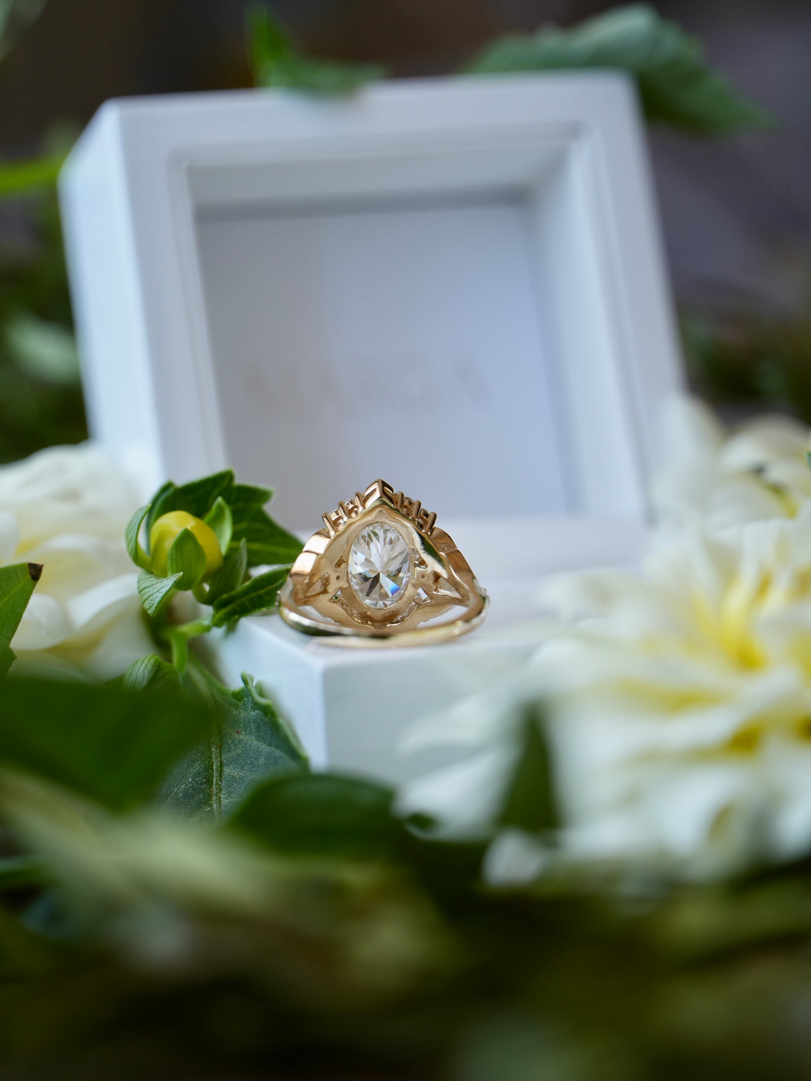 Gold ring with a diamond on a white box surrounded by flowers