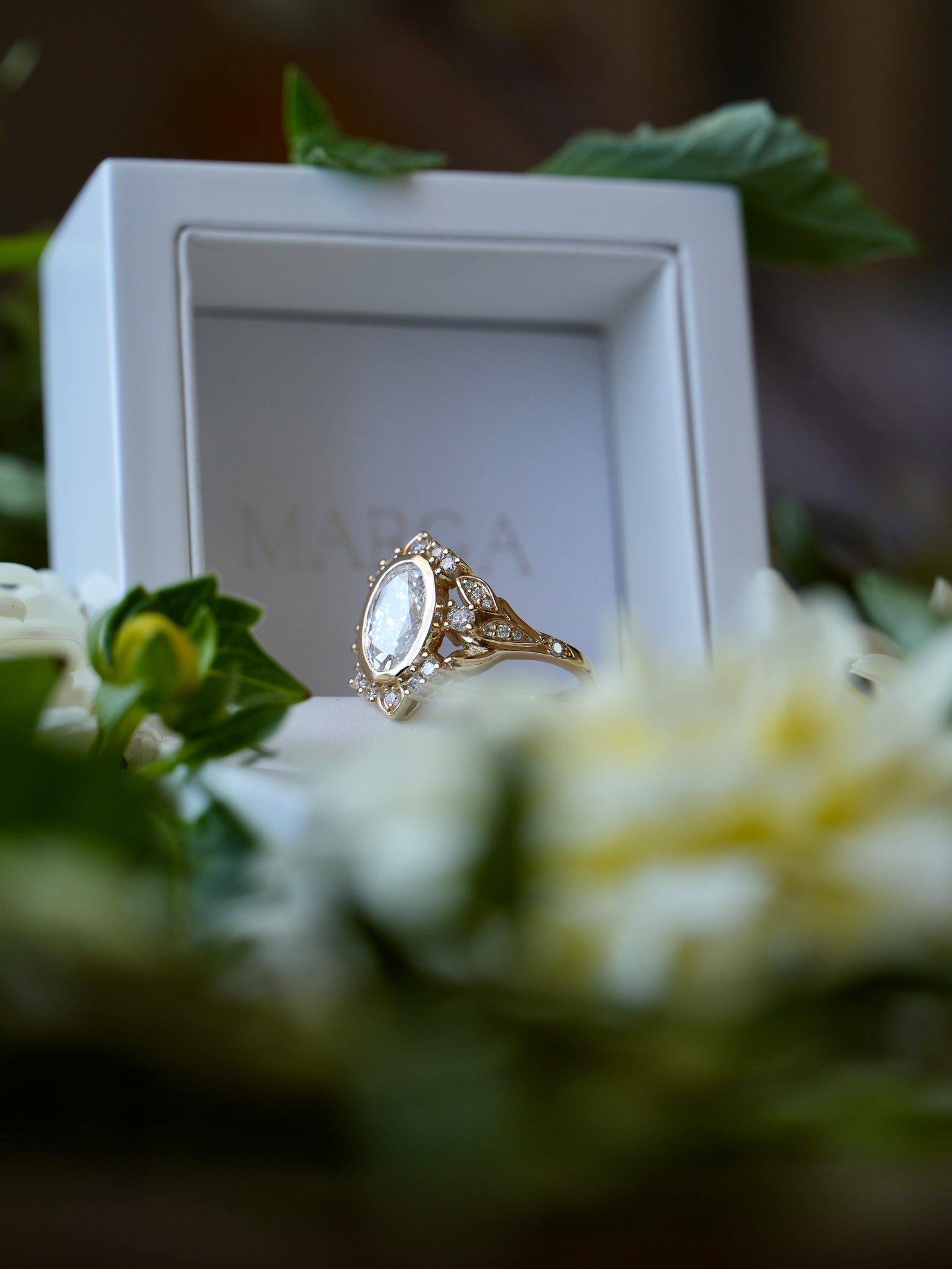 Gold ring with a large gemstone in a white box surrounded by flowers