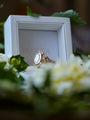 Gold ring with a large gemstone in a white box surrounded by flowers