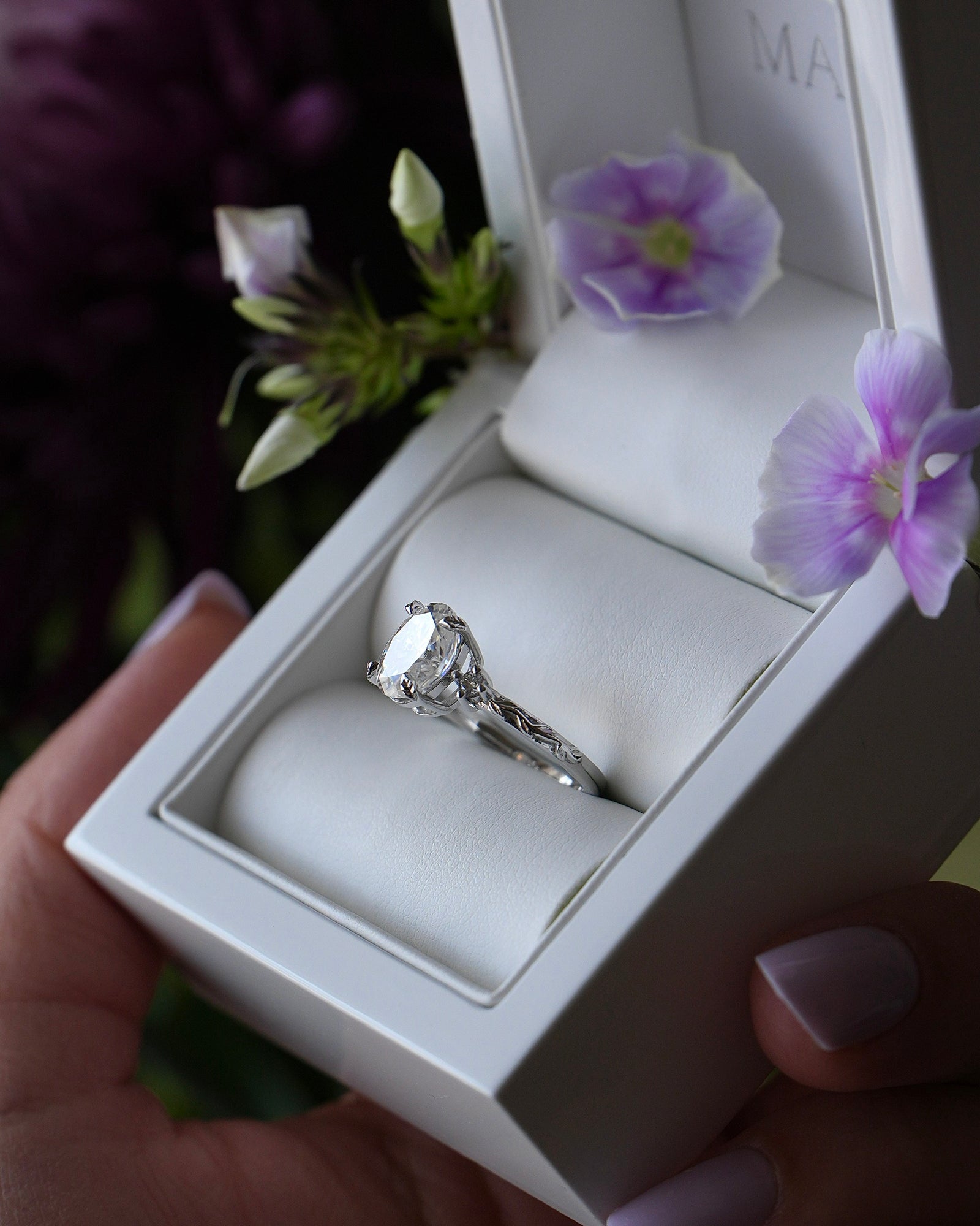 Diamond ring in a white box with purple flowers