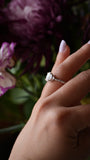 Hand wearing a diamond ring with a blurred floral background