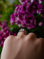 Hand wearing a diamond ring with purple flowers in the background