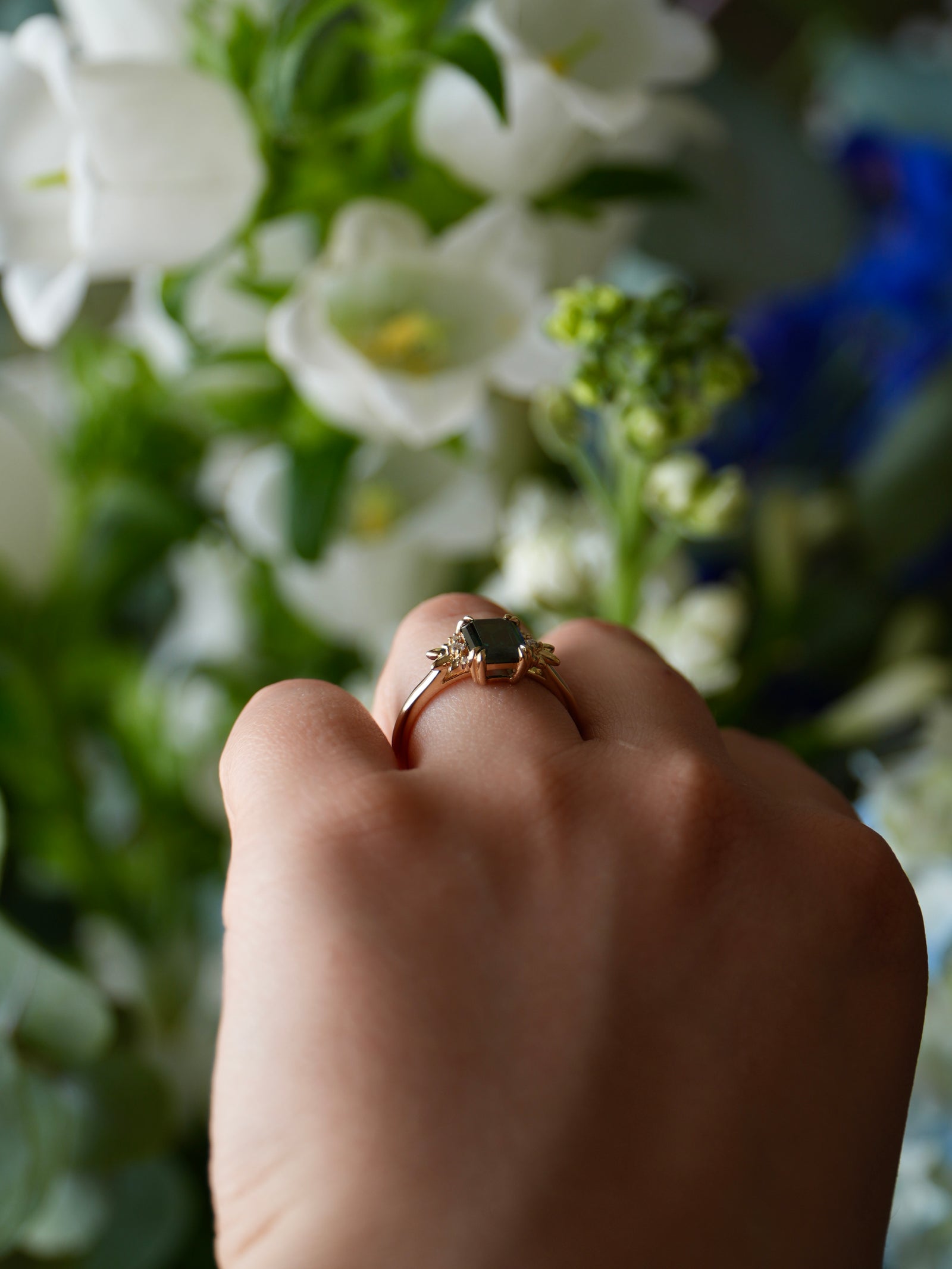 Hand wearing a ring with a black stone against a blurred floral background