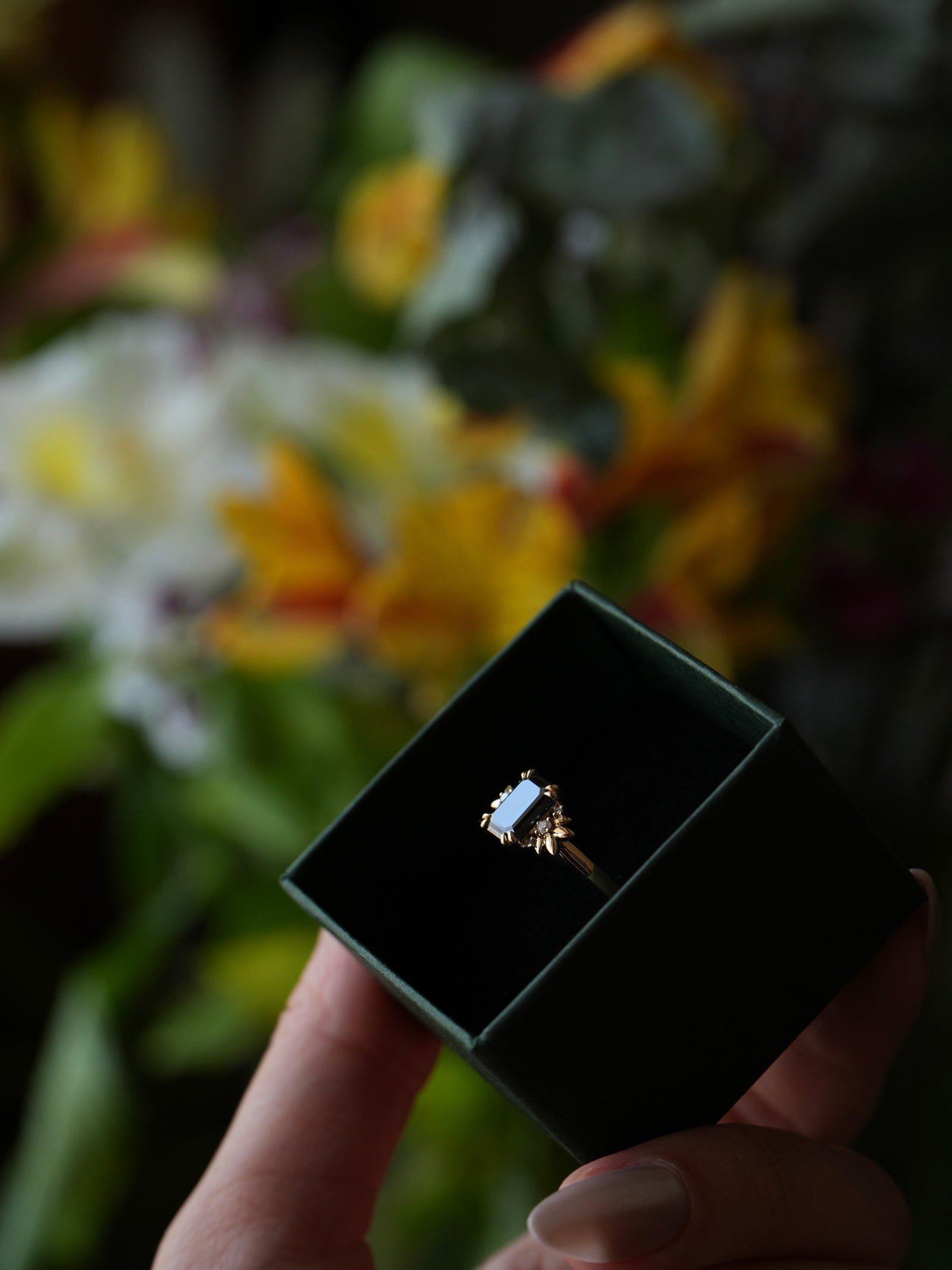 Diamond ring in a box held by a hand with a blurred floral background