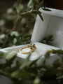 Gold ring with green gemstone on a white surface with blurred green leaves in the foreground