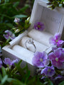 Diamond ring in a white box with purple flowers around