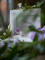 Diamond ring in a white box with 'Mare' branding, surrounded by flowers.