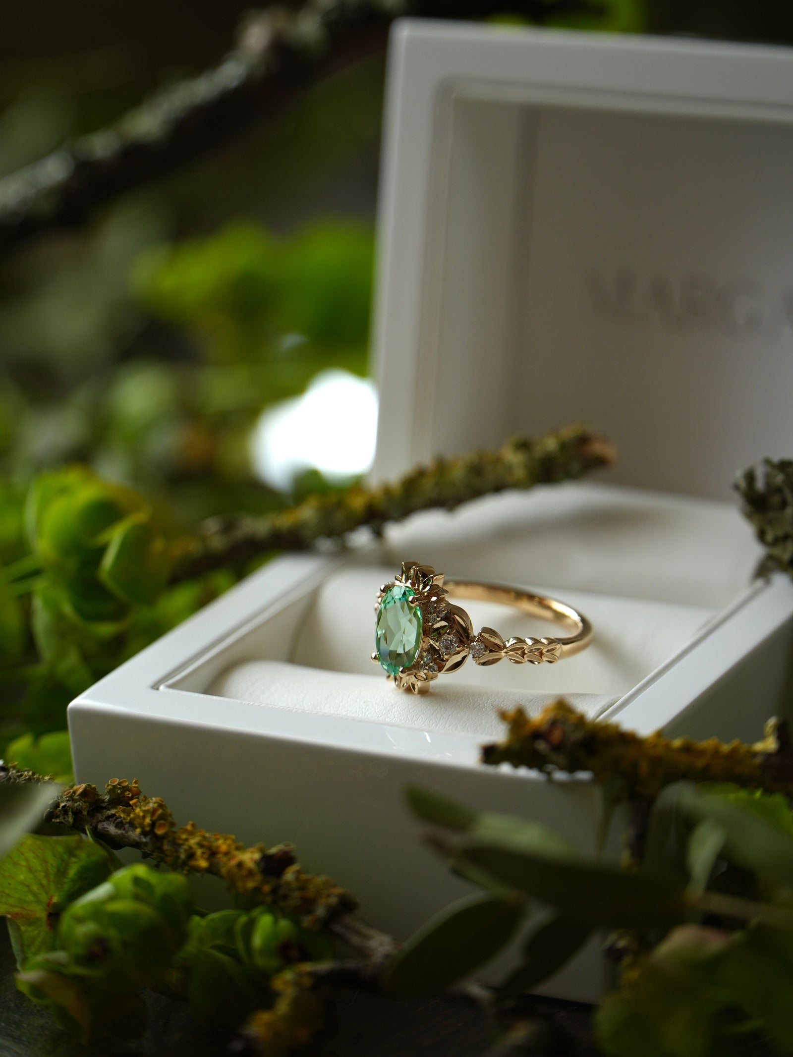 Gold ring with a green gemstone in a white box on a natural background