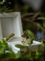 Gold ring with a green gemstone in a white box surrounded by greenery