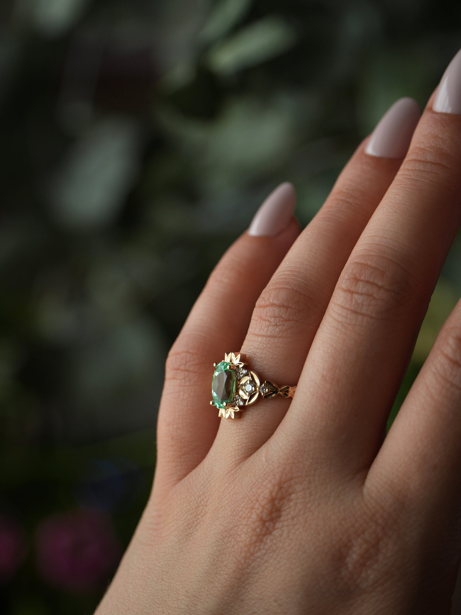 Gold ring with a green gemstone on a hand against a blurred natural background
