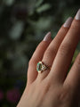 Gold ring with a green gemstone on a hand against a blurred natural background