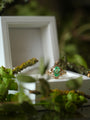 Gold ring with a green gemstone on a white stand surrounded by greenery