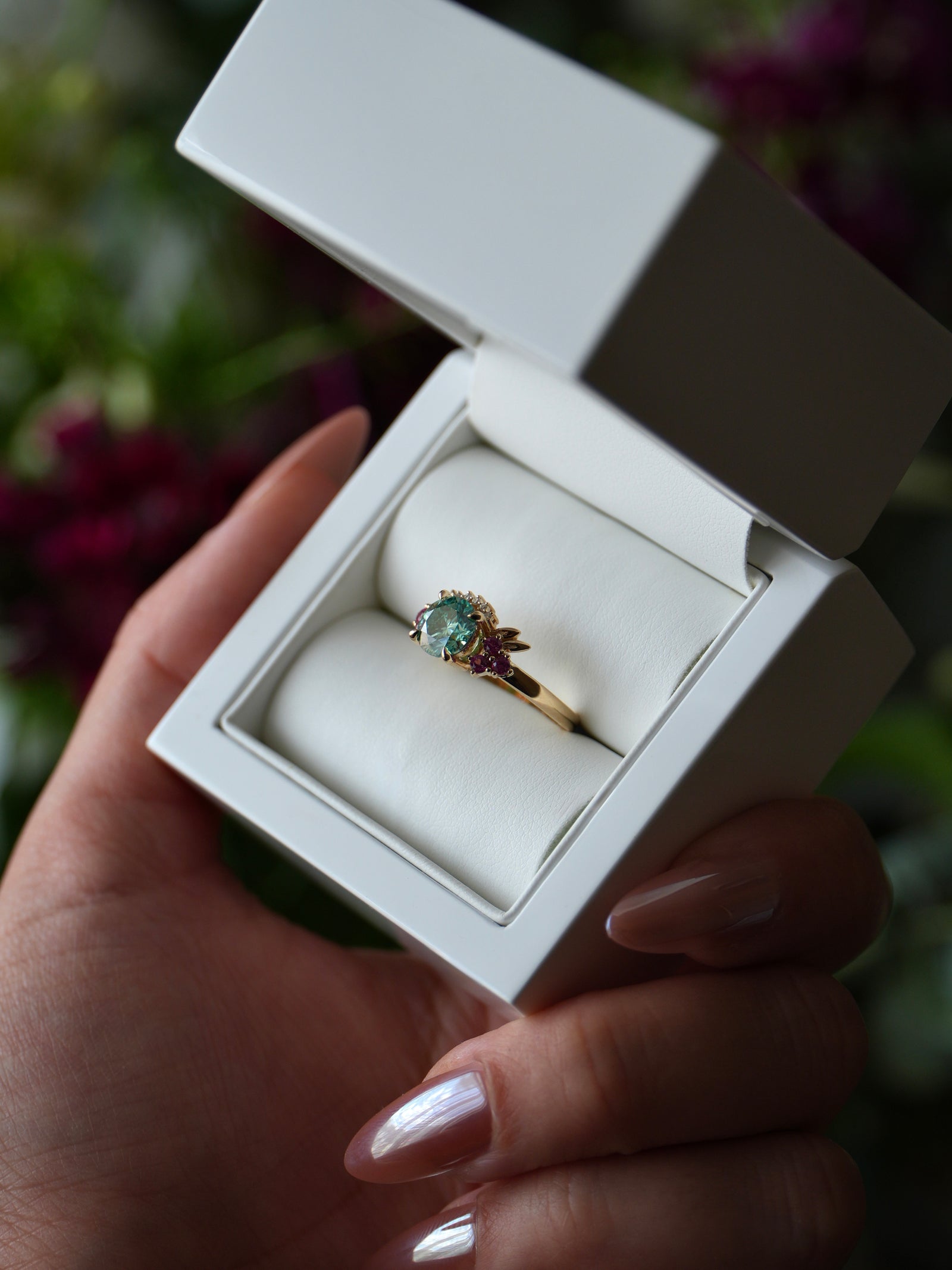 Gold ring with a green gemstone in a white box held by a hand.
