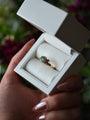 Gold ring with a green gemstone in a white box held by a hand.