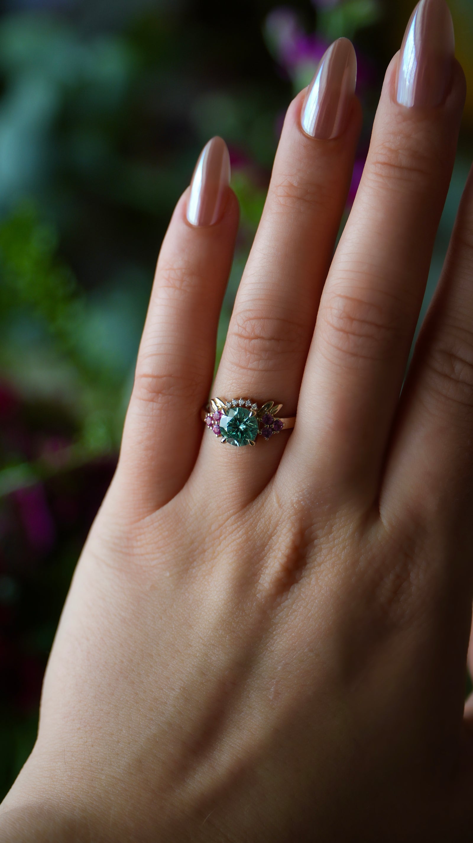 Hand wearing a ring with a green gemstone against a blurred natural background