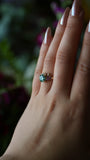 Hand wearing a ring with a green gemstone against a blurred background