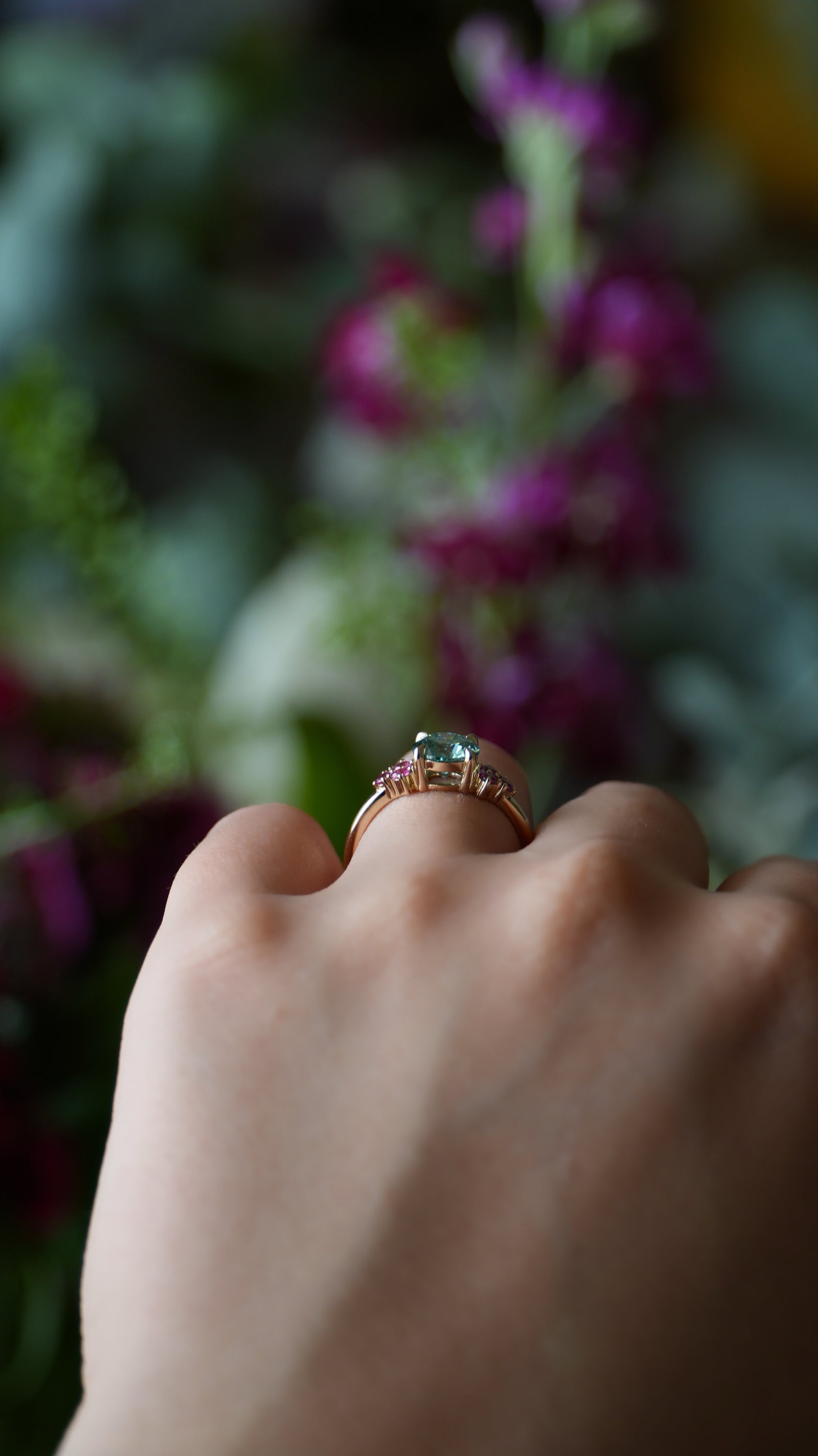 Hand wearing a ring with a green gemstone against a blurred floral background