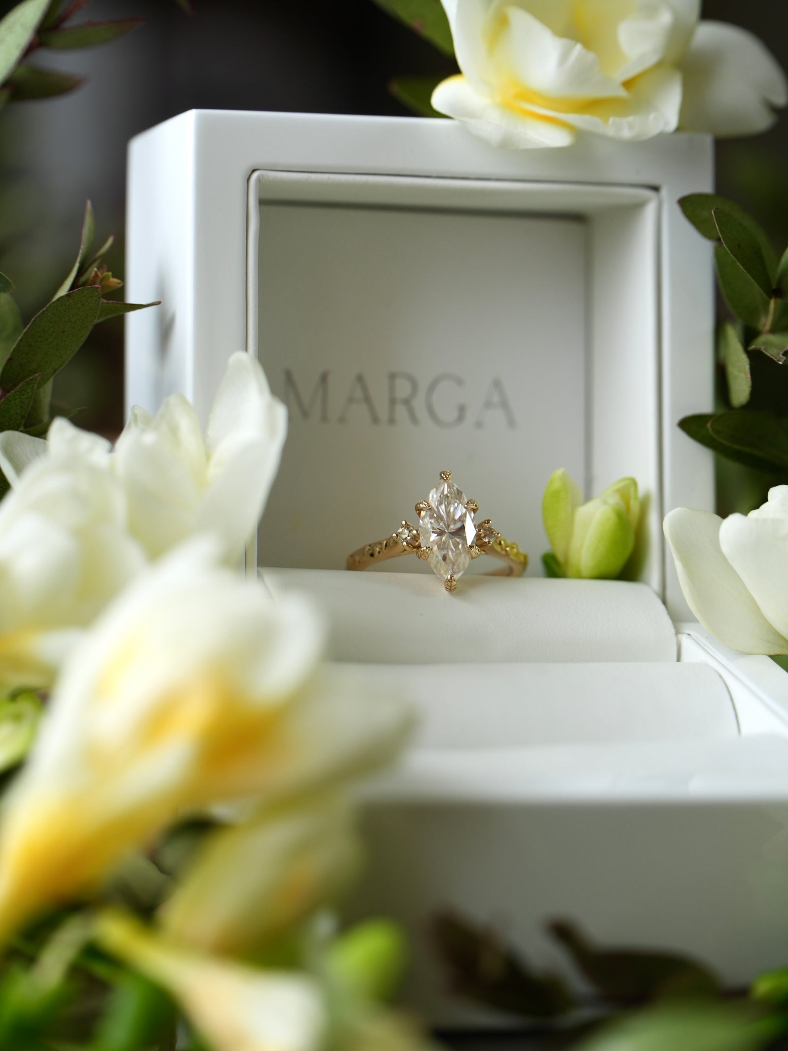 Gold ring with a diamond in a 'MARGA' box surrounded by white flowers