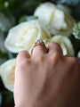Hand wearing a ring with a diamond, held against a background of white flowers.