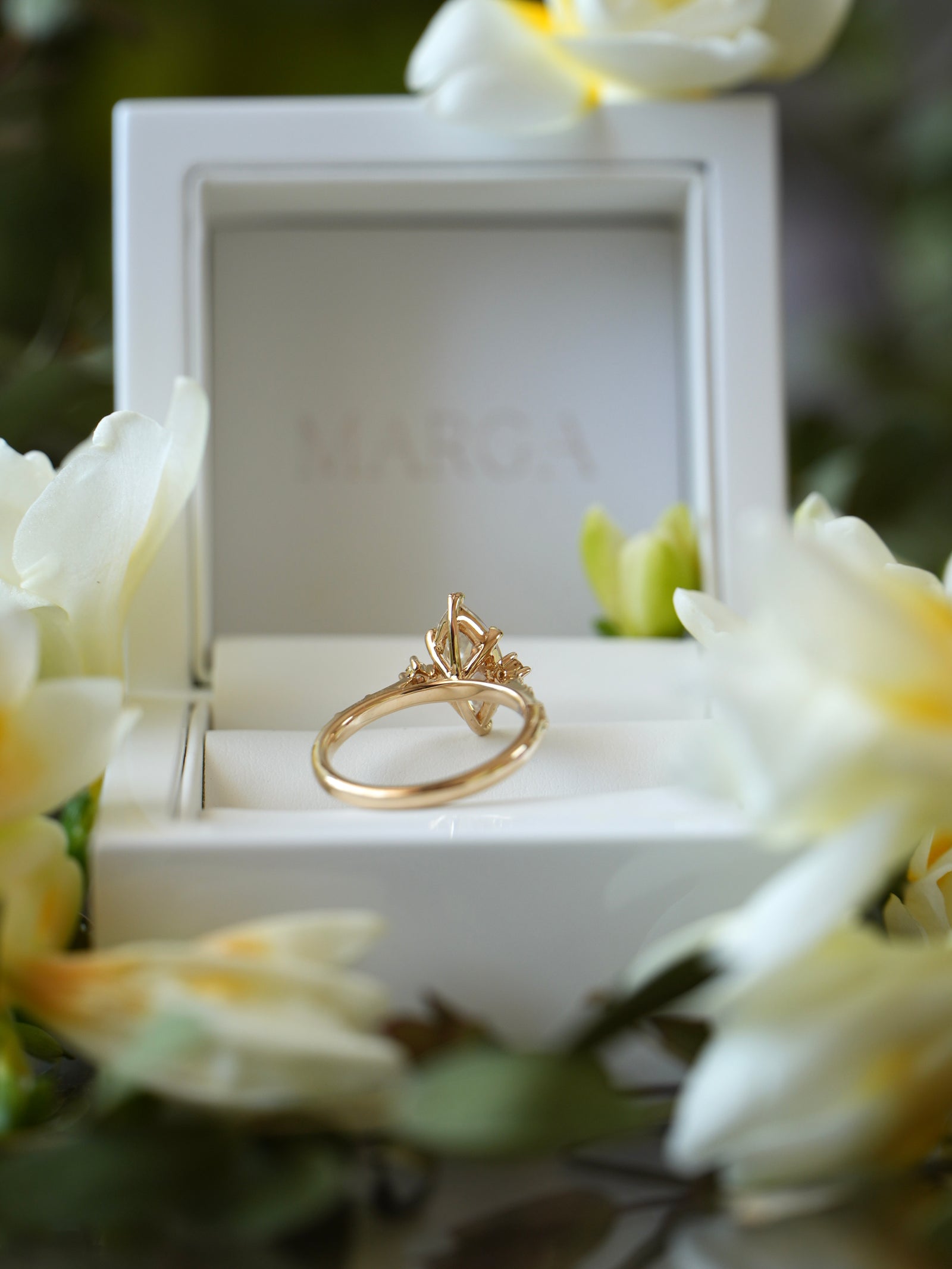 Gold ring in a white jewelry box with flowers around