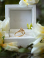 Gold ring in a white jewelry box with flowers around