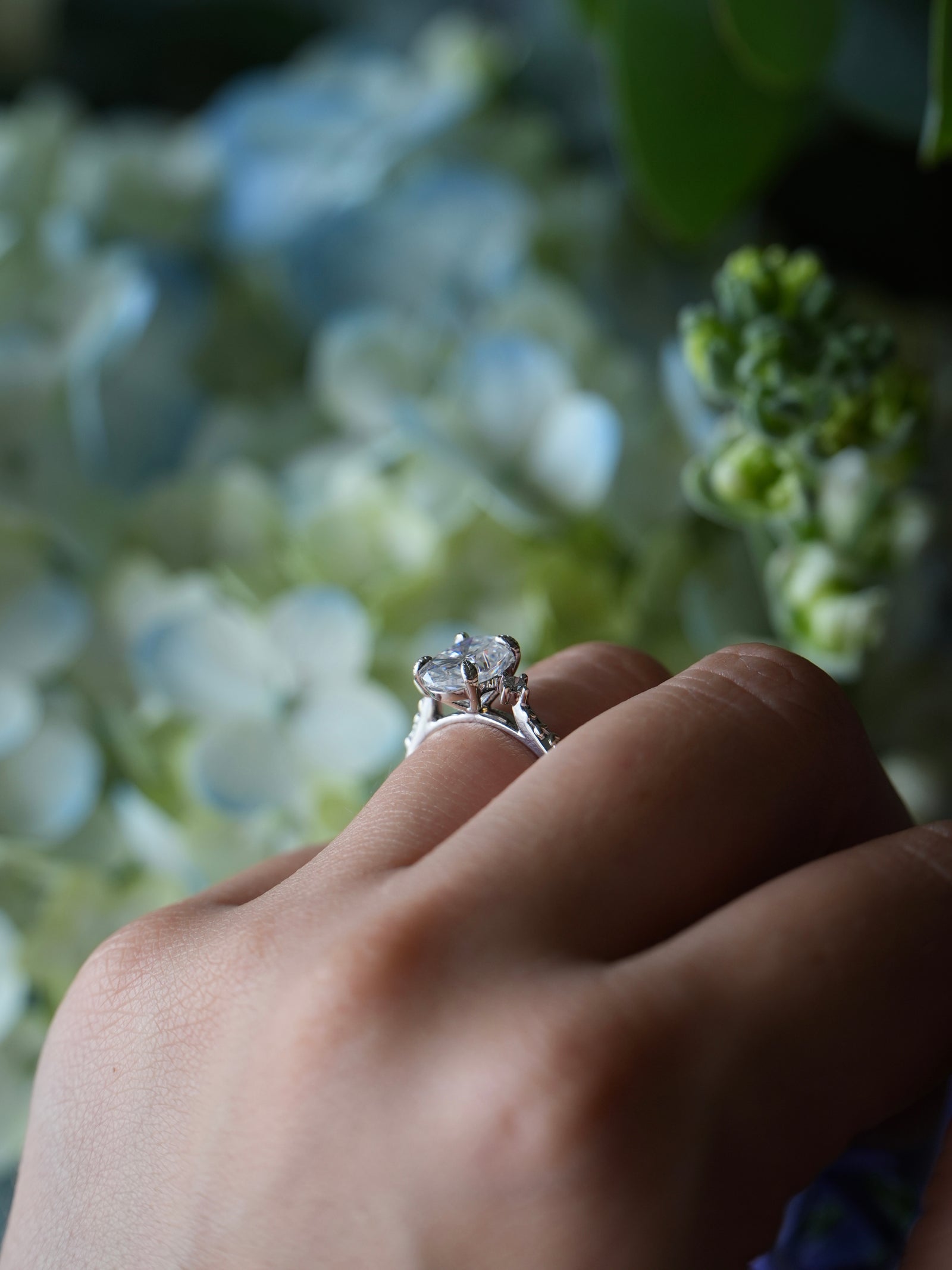 Close-up of a hand wearing a diamond ring with a blurred floral background
