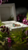 Gold ring with a green gemstone in a white box surrounded by flowers