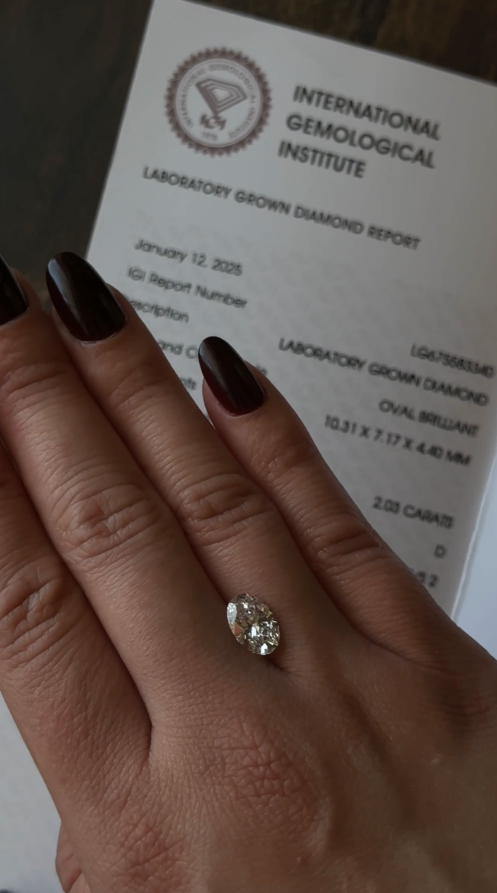 Hand wearing a diamond ring with an International Gemological Institute report in the background