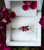 Ring with gemstones in a white box surrounded by pink flowers