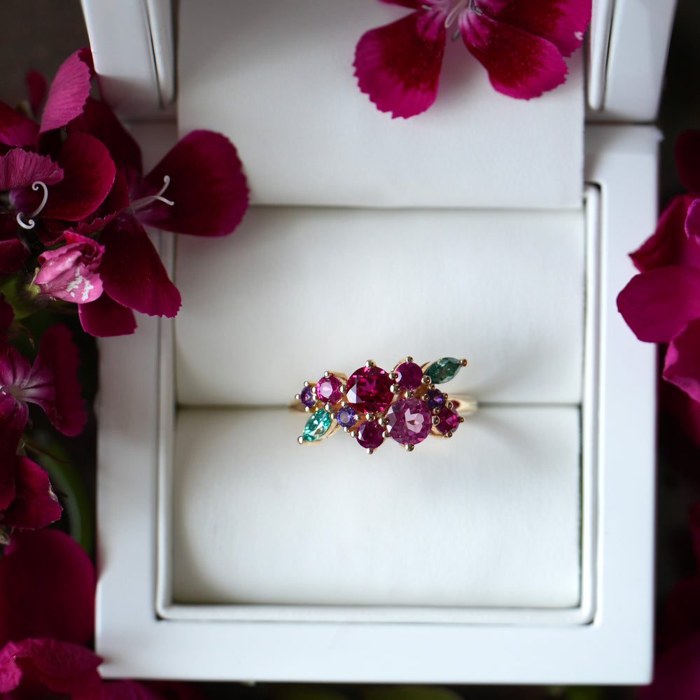 Ring with gemstones in a white box surrounded by pink flowers