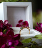 Gold ring with gemstones in a white box surrounded by purple flowers