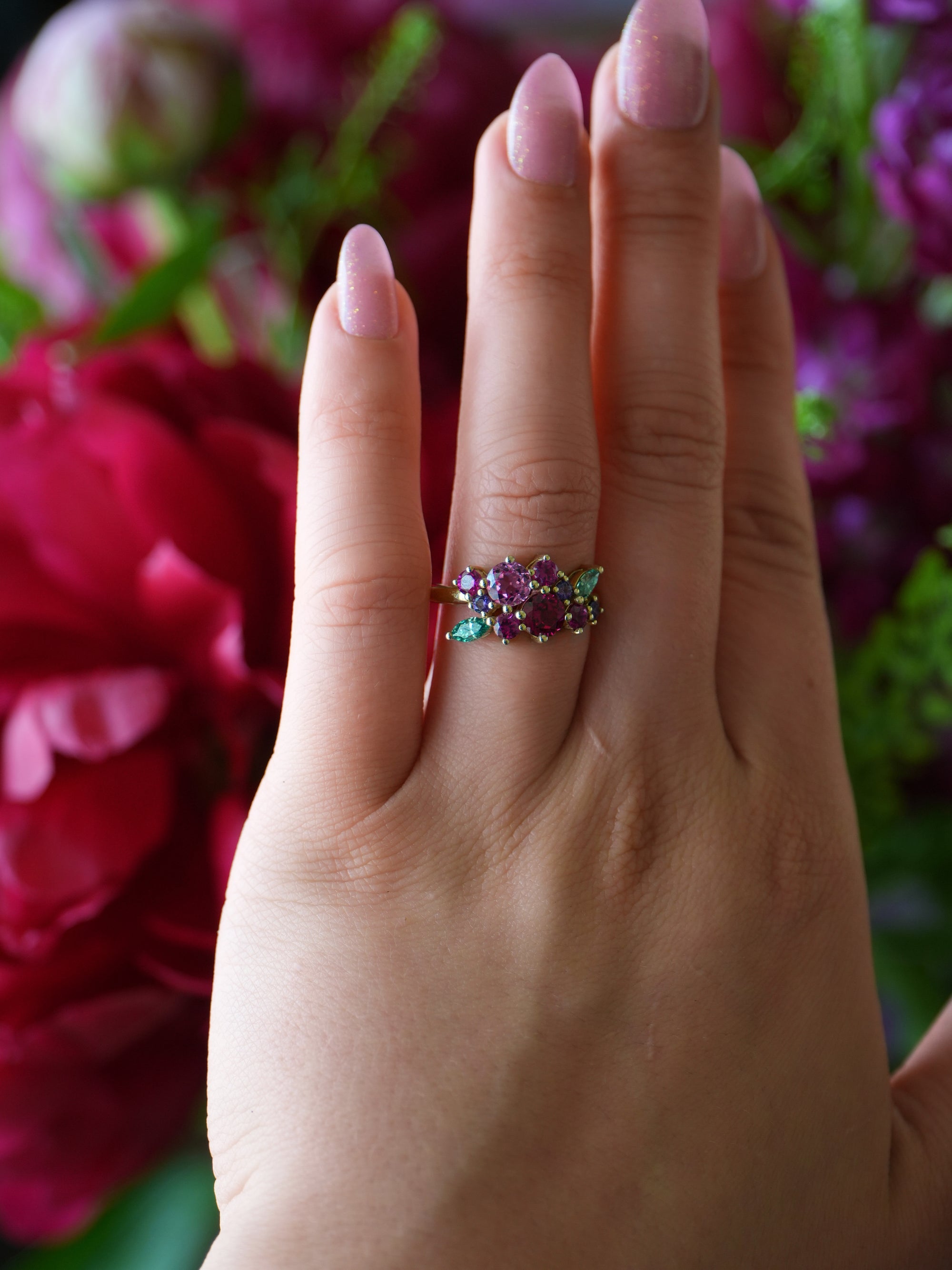 Hand wearing a colorful ring with flowers in the background