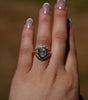 Close-up of a hand wearing an ornate ring with a large gemstone against a blurred background