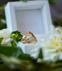 Gold ring with a diamond on a white box surrounded by flowers