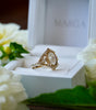 Gold ring with diamonds in a white box surrounded by white flowers