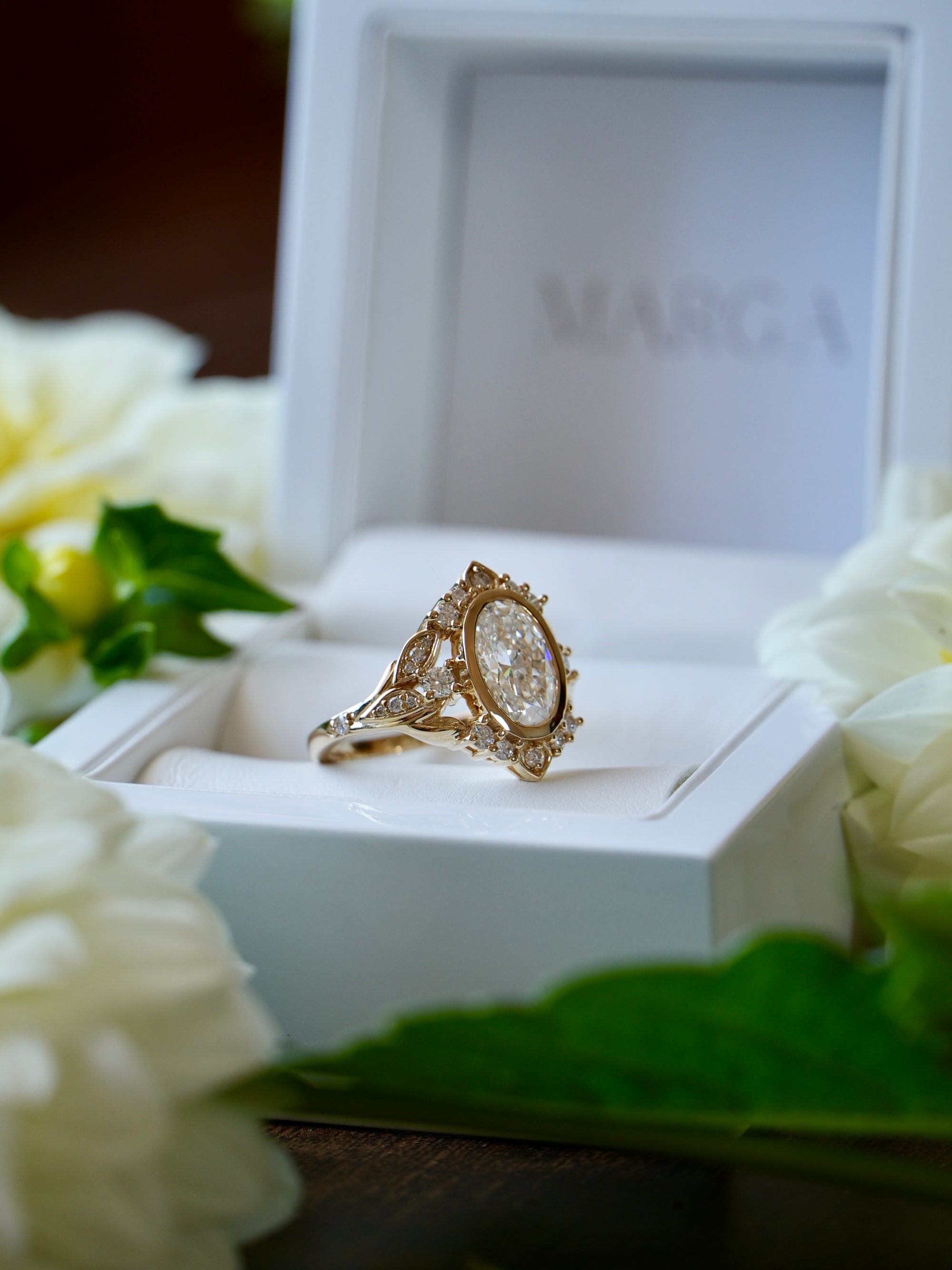 Gold ring with diamonds in a white box surrounded by white flowers