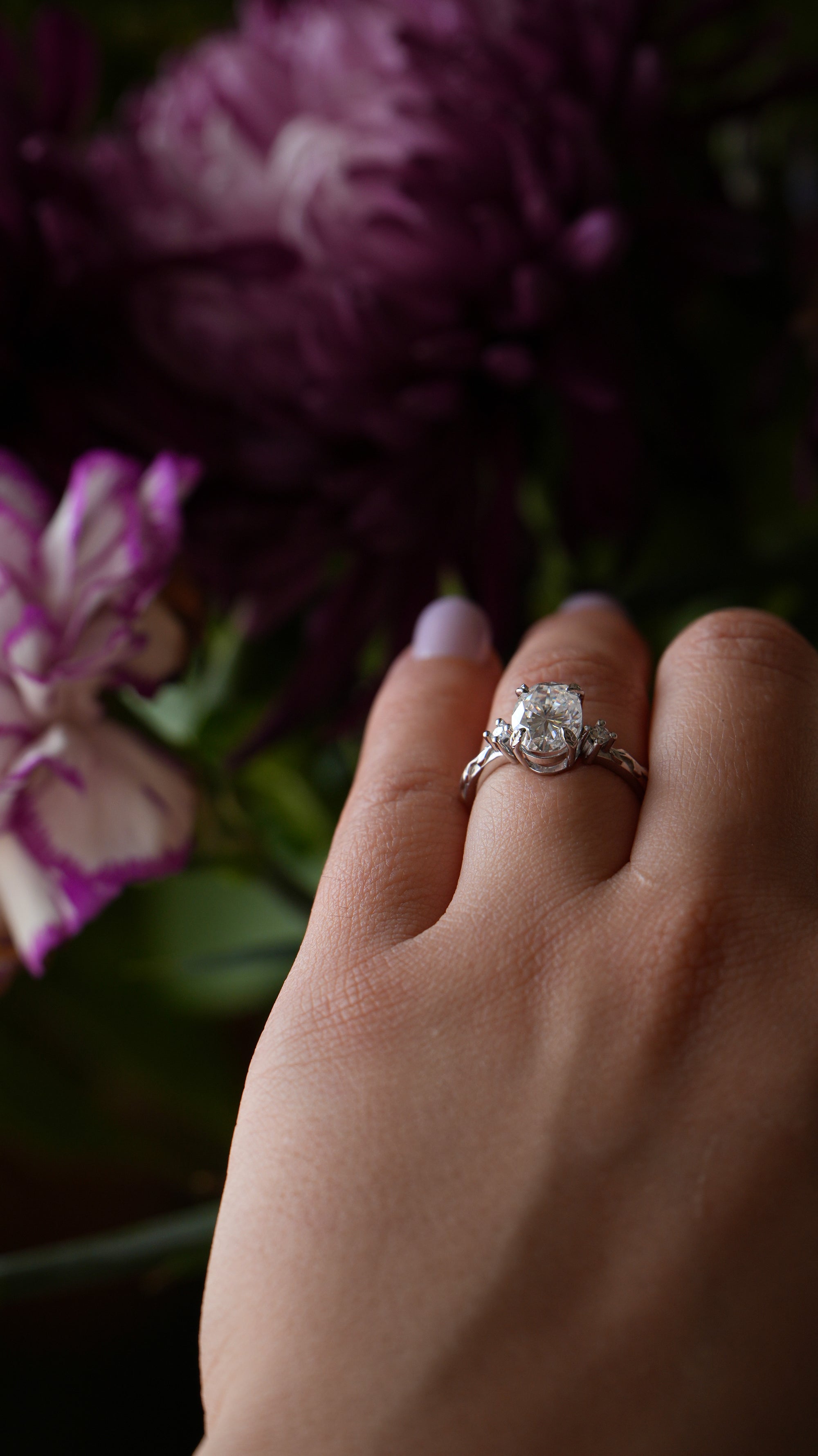 Hand wearing a ring with a diamond, surrounded by purple flowers