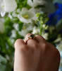 Hand wearing a ring with a black stone against a blurred floral background