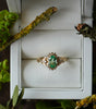 Gold ring with a green gemstone in a white box surrounded by greenery