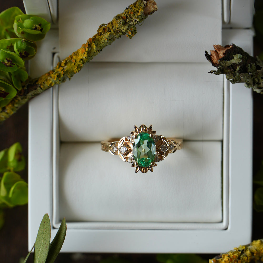 Gold ring with a green gemstone in a white box surrounded by greenery