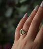 Gold ring with a green gemstone on a hand against a blurred natural background