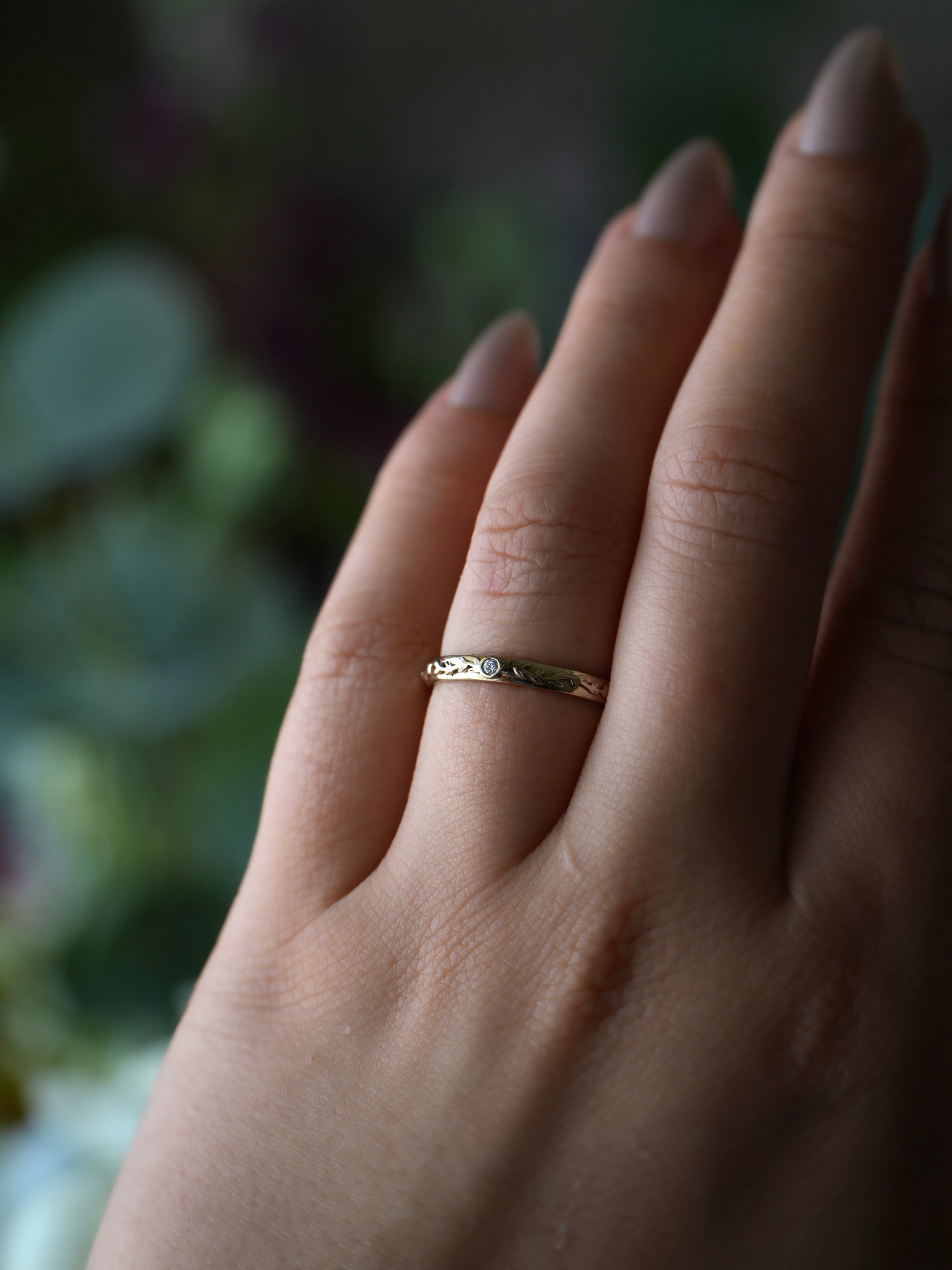 Close-up of a hand wearing a gold ring with a blurred natural background