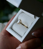 Gold ring with a diamond in a white box held by a hand.