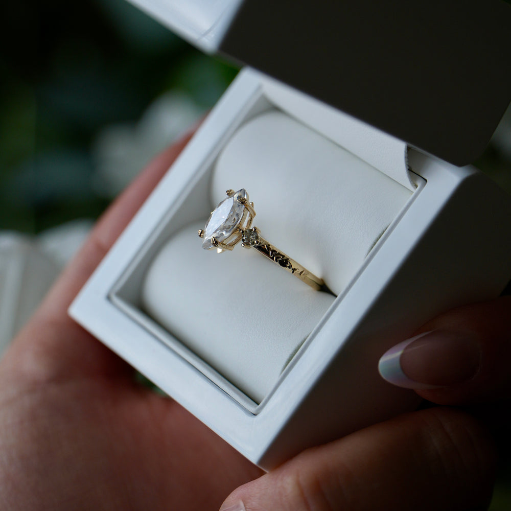 Gold ring with a diamond in a white box held by a hand.