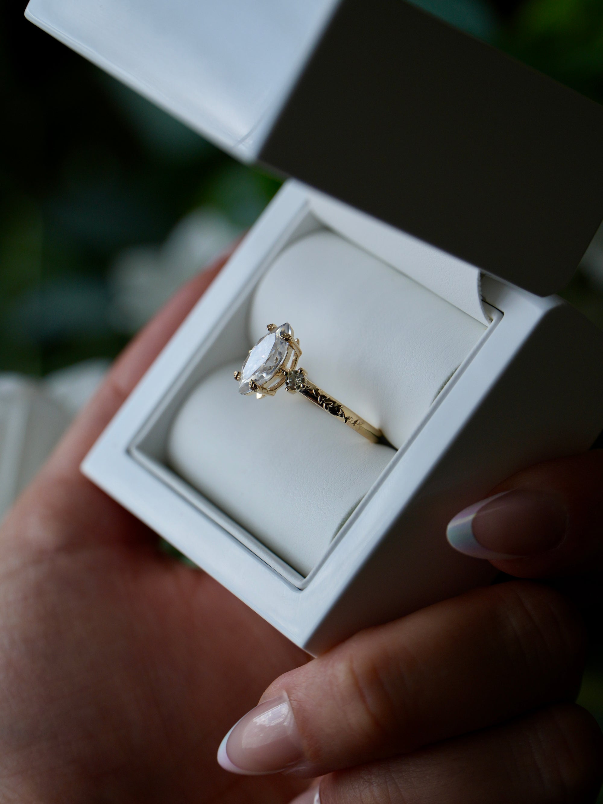 Gold ring with a diamond in a white box held by a hand.