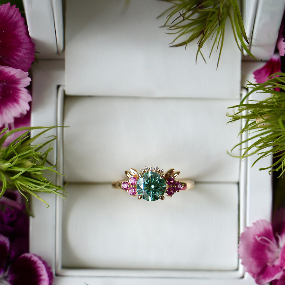 Ring with gemstones in a jewelry box surrounded by flowers and greenery