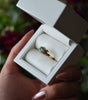 Gold ring with a green gemstone in a white box held by a hand.